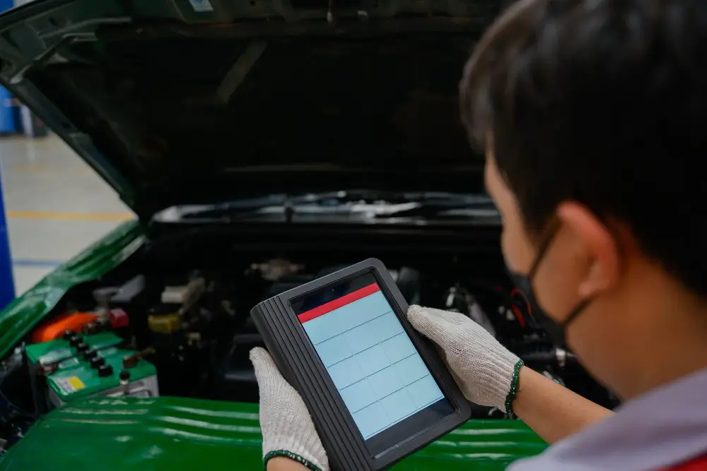 Technicien consultant une tablette de diagnostic devant un capot ouvert